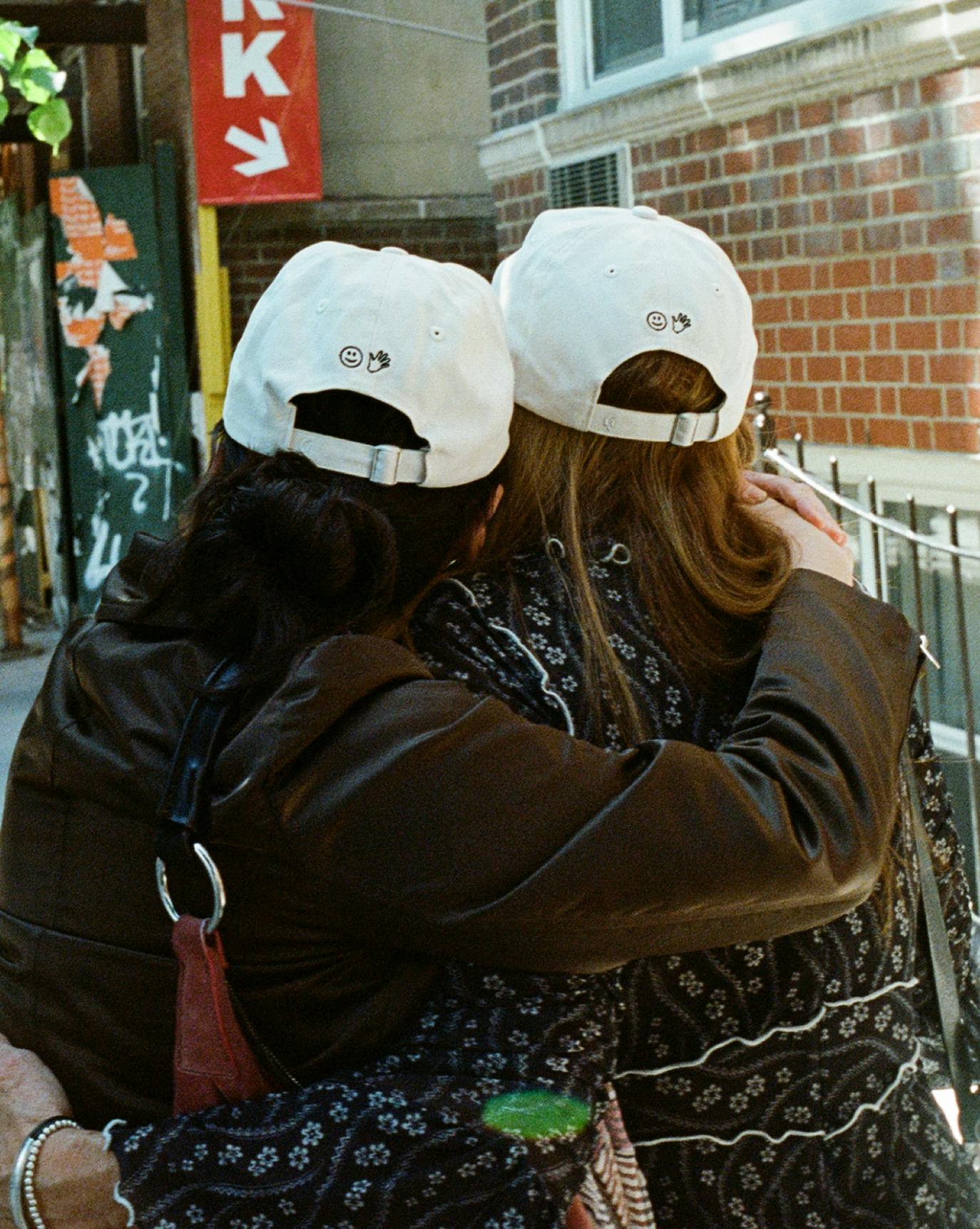two friends wearing you look good cap embracing